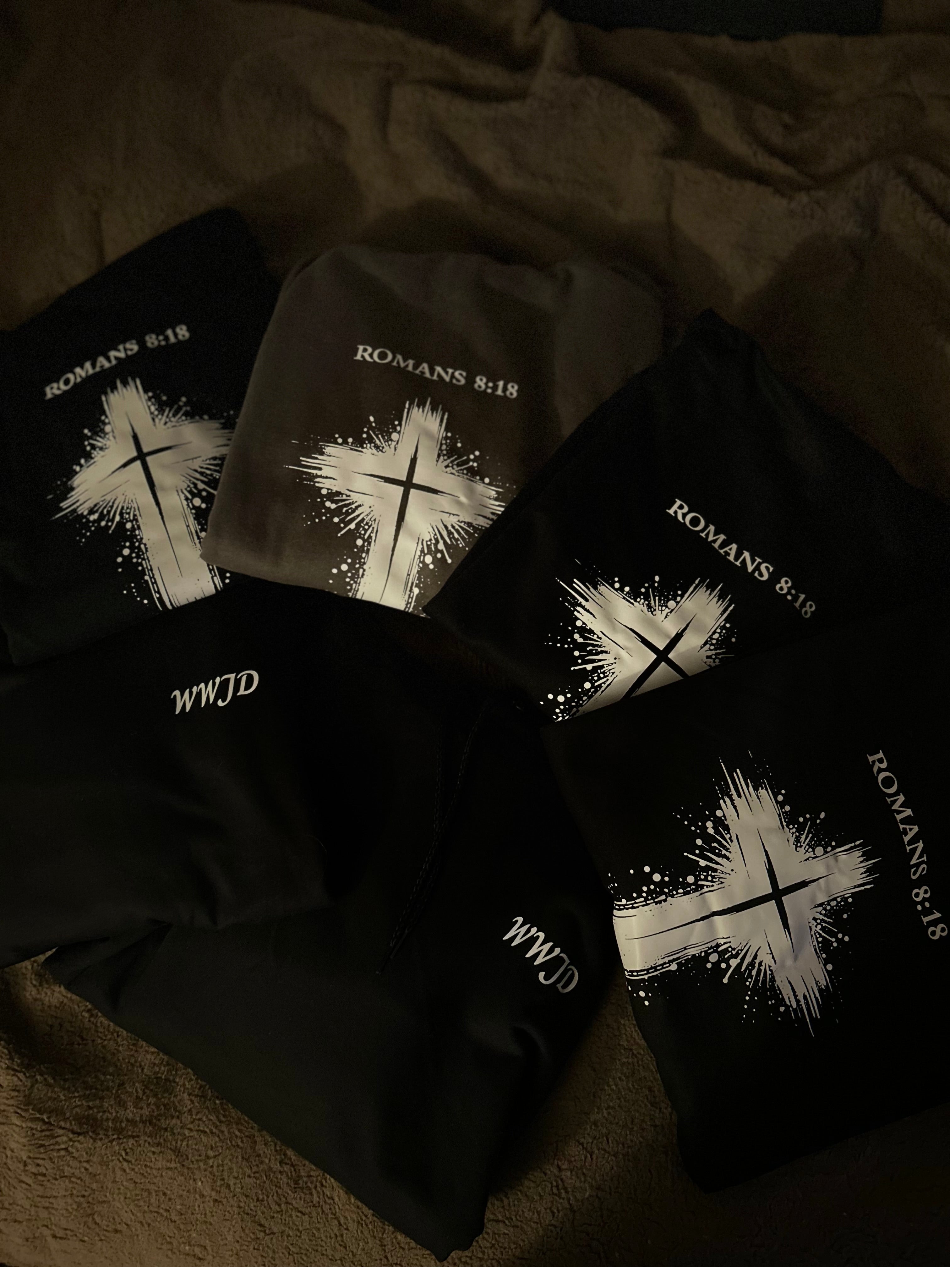 Black sweatshirts with cross designs and text on a dark surface